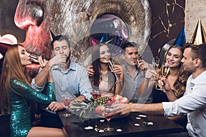 Young people are resting in a trendy nightclub. They clink glasses and drink champagne.
