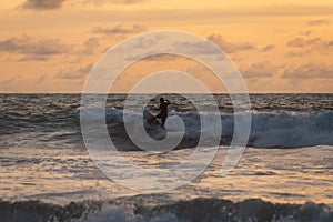 Young people ride on short boards, perform bright tricks on the waves during sunset.