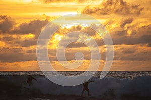 Young people ride on short boards, perform bright tricks on the waves during sunset.