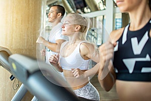 Young people running on a treadmill at gym.