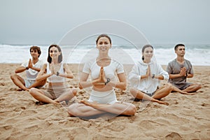Young people& x27;s beach meditation practices. Group of men and women meditating on ocean shore