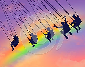 Young people are seen riding a carousel chair swing  with a colorful rainbow in the sky