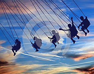 Young people are seen riding a swing chair ride with a beautiful sky