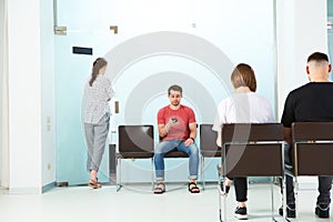 Young people sit in line to see a doctor at a clinic reading the news on their smartphones.