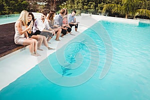 Young people sitting by swimming pool