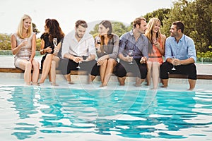 Young people sitting by swimming pool
