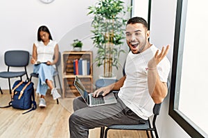 Young people sitting at waiting room working with laptop celebrating victory with happy smile and winner expression with raised