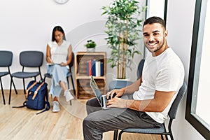 Young people sitting at waiting room working with laptop looking positive and happy standing and smiling with a confident smile