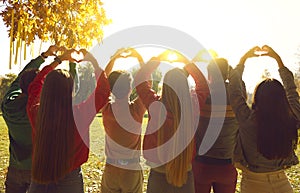 Young people standing in autumn park at sunrise and forming heart shapes with hands