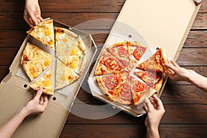 Young people taking slices of hot cheese pizzas from cardboard boxes at table, top view.