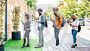 Young people waiting in line practising social distancing at city shop - New normal lifestyle concept with people wearing facemask