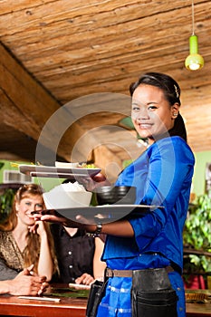 Young people with waitress eating in Thai restaurant