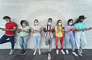 Young people wearing face mask using mobile smartphone outdoor - Multiracial friends having fun with new technology social media