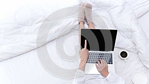 Young people working on laptop and drinking coffee in morning relax mood in winter season. Close up legs women on white bed