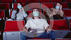 Young peoplein medical masks laughing at cinema theater. Media. Joyful Cheerful audience watching amusing comedy in