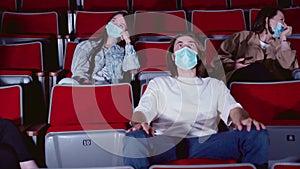 Young peoplein medical masks laughing at cinema theater. Media. Joyful Cheerful audience watching amusing comedy in