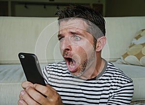 Young perplexed and shocked man using mobile phone looking internet social media or checking news in surprised and crazy disbelief