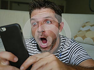 Young perplexed and shocked man using mobile phone looking internet social media or checking news in surprised and crazy disbelief