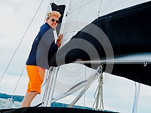 Young person a crew member lowering sail on sailing yacht because rain and storm begin