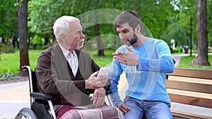 Young person explaining disabled pensioner how to use smartphone outdoors