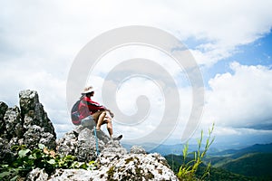 Young person hiking female sitting on top rock, Backpack woman looking at beautiful mountain valley at sunlight in summer,