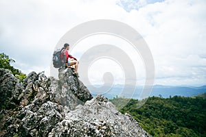 Young person hiking female sitting on top rock, Backpack woman looking at beautiful mountain valley at sunlight in summer,