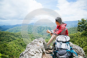 Young person hiking female sitting on top rock, Backpack woman looking at beautiful mountain valley at sunlight in summer,