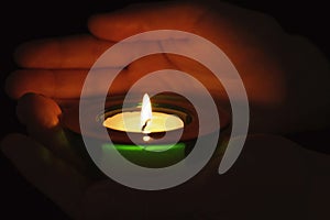 Young person holding burning candle in darkness