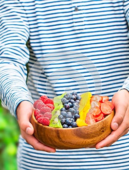 A young person holding up a large bowl of fresh berries and frui