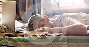 Young person lying and sleeping on the bed in the sunny morning after working on laptop in the night f photo