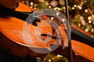 A young person playing the violin with a Chrismas tree in the background