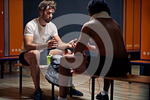 Young personal trainer with his client sitting in dressing room, facing each other, talking