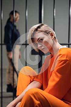 A young pert blonde with piercings is in jail for a cyber crime. Head portrait on the background of a prison cell.