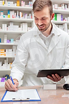 Young pharmacist holding a tablet and filling out paperwork on a clipboard