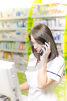 Young pharmacist woman expressing wonder while having a phone call. Pharmaceutical background. Drugstore. Pills and medicine.