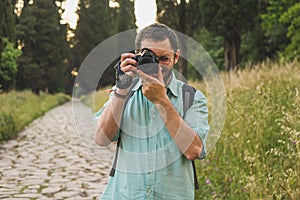 Young photographer focusing and taking a picture towards the camera in the park