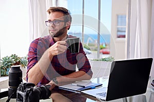 Young photographer holding coffee at his work desk