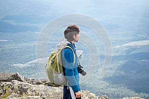 Young photographer in sun light stands on the top of a mountain