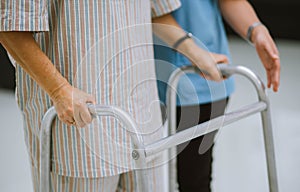 young physical therapist helping senior patient in using walker during rehabilitation