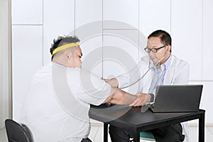 Young physician checks heartbeat of his fat patient