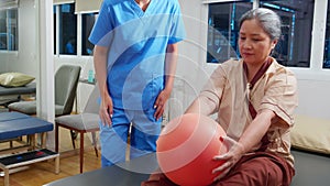 Young physiotherapist assistance elderly patient while guidance therapy with lift ball in room at hospital or rehab.