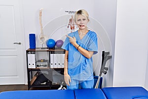 Young physiotherapist woman working at pain recovery clinic pointing aside worried and nervous with forefinger, concerned and