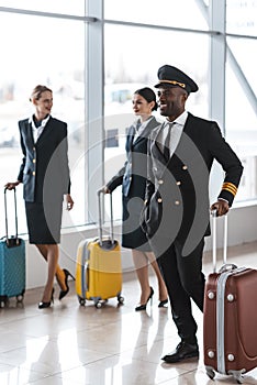 young pilot and stewardesses with luggage walking