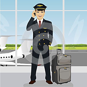 Young pilot talking on phone with luggage in front of an airport observation deck