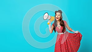 Young pin up woman in retro dress shouting into megaphone, making announcement on blue studio background, banner