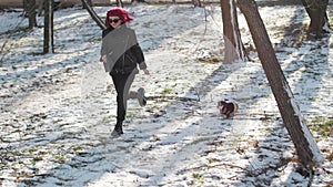 young pink-haired woman walking with funny puppy in winter snowy weather