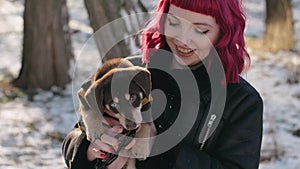 young pink-haired woman walking with funny puppy in winter snowy weather