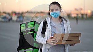 Young pizza courier is delivering an order. Delivery woman holding cardboard boxes in medical mask