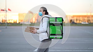 Young pizza courier is delivering an order. Delivery woman holding cardboard boxes in medical mask