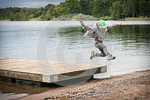 Young playful caucasian boy running in mid-air making a jump from a jetty to the beach.